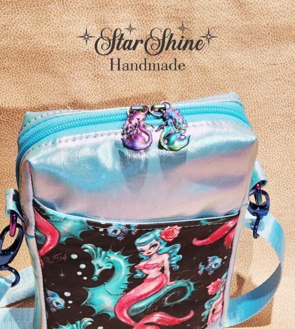 Small crossbody blue bag with a mermaid design on it. Top zipper with rainbow mermaid zipper pulls